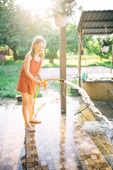 a girl in an orange overall plays with a dog in the garden, watering with water from a hose. backlight summer photo