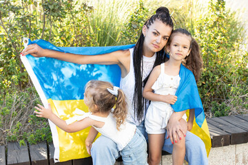 Ukrainian mother with two girls with flag of Ukraine. Outside. Concept of problem of war in Europe,...