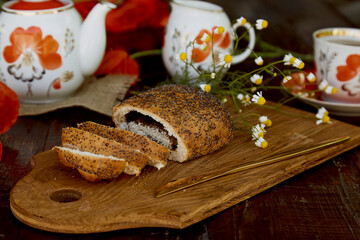 Traditional poppy seed bun with cup of tea and milk near poppies flowers and dishes with poppies ornaments. Delicious breakfast in summer. Lifestyle photography