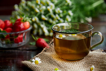 Organic chamomile, mint tea, herbal infusion tea, antioxidant. Fresh strawberries, chamomile flowers and mint on wooden table. Natural summer breakfast. Aesthetic summer lifestyle. Beautiful food
