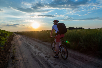 Fototapeta na wymiar cyclist riding a bike at sunset. concept of extreme cycling. man driving bicycle on the way to the field in the summer.