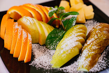 a plate with pieces of pear, apple and orange with powdered sugar and mint. beautiful dessert serving and table setting.