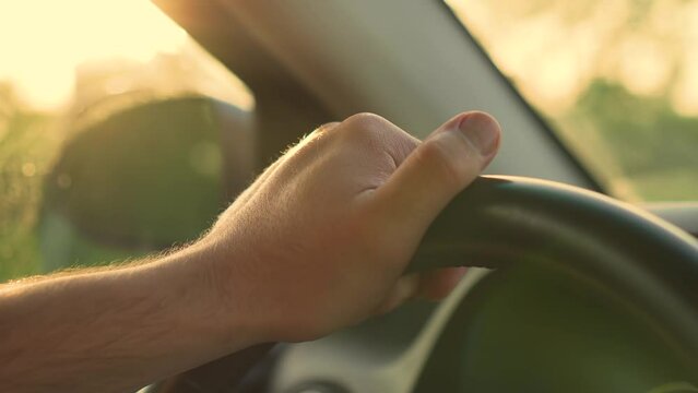 Close up of man's hand on steering wheel of car while driving at sunset. Concept of traveling and free lifestyle