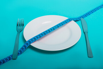 Healthy food, fitness for weight loss. An empty plate with a forkknife measuring tape in centimeters on a blue background from above. Diet menu Obesity. Place for an inscription. Advertising. - 514610575