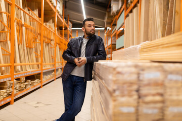 Fototapeta premium a male customer in a hardware store stands in the lumber department leaning on a rack with boards