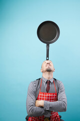 A bald caucasian man in suit balancing an frying pan on his head isolated on blue background.