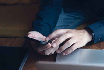 Man working on laptop and using mobile phone with digital tablet on wooden table at coffee shop, telecommuting, closeup