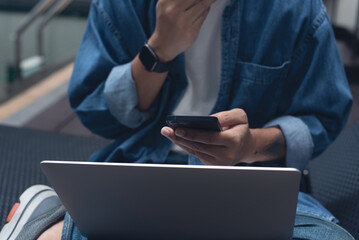 Technology and people lifestyle concept. Man freelancer sitting cross legged using mobile phone and laptop computer outdoors. Man online working and surfing the internet, close up