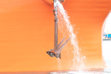 Fototapeta na wymiar Big rusty anchor on orange with water flowing out of the boat ship in the harbor. At a large port in Thailand. The anchor of a large cargo ship is flowing into the sea to dock for exports and imports.