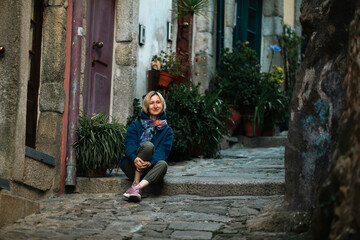 A woman sits on the steps a narrow street in Porto, Portugal.