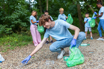 Hand of man picking up bottle into garbage bags while cleaning area in park. Volunteering, charity, people, ecology concept. Closeup volunteer collecting plastic trash in forest. World clean up m day