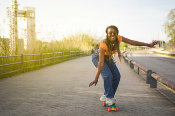 young afro black woman having a ride on her skateboard near the river in downtown at sunset looking at camera, copy space © Guirado