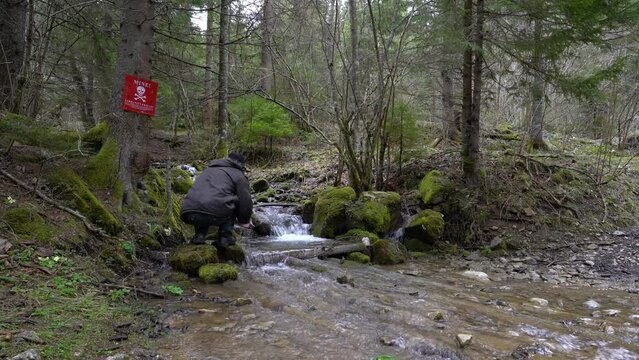 A man washes his hands in forest creek near a mined area - (4K)