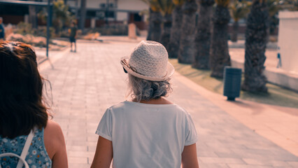 mujer con un sombrero blanco paseando por un paseo de la costa en pleno verano