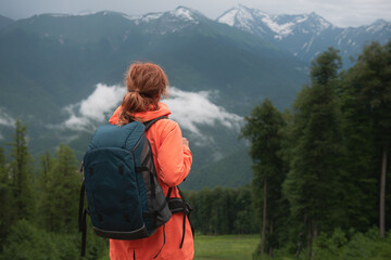 Fototapeta na wymiar Young woman traveler with backpack hiking in the mountains. Summer landscape of the mountains and forest. Travel and adventure concept