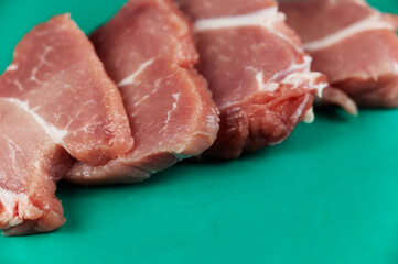 Raw pork is cut crosswise into portioned pieces. Four portioned pieces of pork shoulder. Raw meat lies on a green wet surface. Food, ingredients. Selective Focus