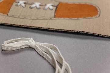 Card for tying laces is against gray background. White shoelace is inserted into the eyelets. The...