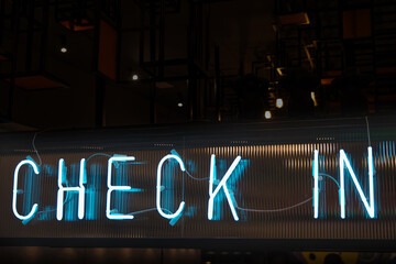 A light blue-colored neon sign saying 'check in' on a dark background. A stylish abstract scene,...