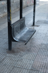 Steel-made bench at a bus stop in Athens, Greece. Graffiti painting on the poles of the roof and general used and aged condition. 