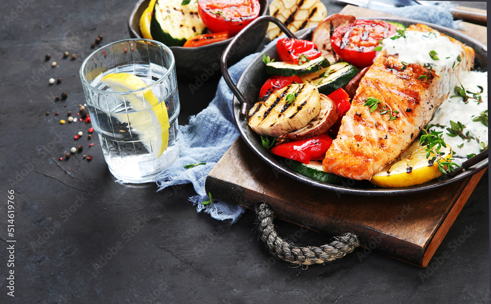 Canvas Prints Salmon steak with vegetables and white sauce on dark background.