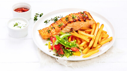 Salmon steak with vegetables and fries on light background.