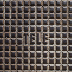 Closeup of iron lid with square pattern and marked with word tele.