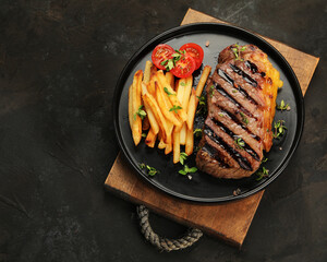 Striploin beef steak with french fries on dark background.