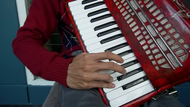 A well-dressed man is sitting on a chair and playing a red accordion traditional musical instrument on the terrace of the house