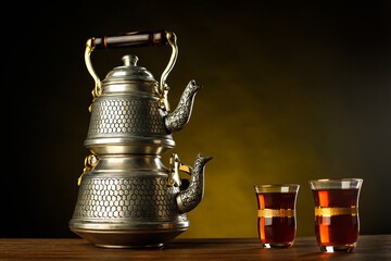 A still-life with Turkish double teapot, authentic glasses and sweets on a dark brown background....