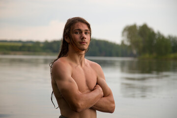 Portrait of a village teenage boy in the river. A long-haired teenager lives harmoniously in nature.