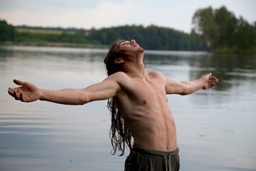Portrait of a village teenage boy in the river. A long-haired teenager lives harmoniously in nature.