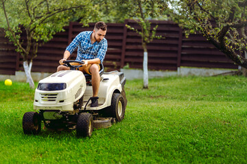 Professional gardener and lawn mower cuts the grass using tractor. Industrial landscaping works - obrazy, fototapety, plakaty