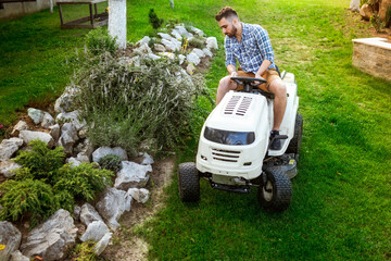 professional gardener doing landscaping works - driving and cutting grass with tractor in a garden....