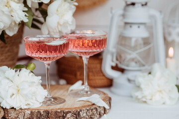 A bouquet of white peonies, flower petals, candles and a fashionable glass for dessert and champagne with a pink drink inside. The concept of a party and a holiday.