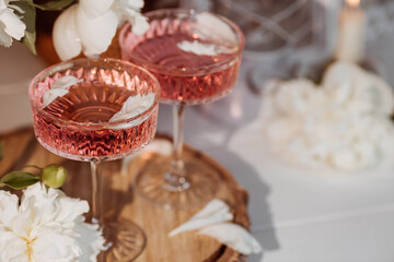 A bouquet of white peonies, flower petals, candles and a fashionable glass for dessert and champagne with a pink drink inside. The concept of a party and a holiday.