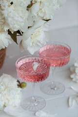 A bouquet of white peonies, flower petals, candles and a fashionable glass for dessert and champagne with a pink drink inside. The concept of a party and a holiday.