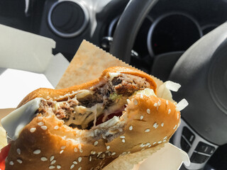 Eating while driving: a bitten burger in the hands inside the car. Steering wheel background