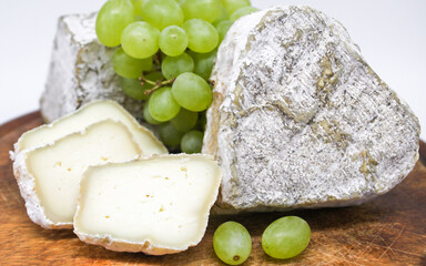 Assorted mouldy blue cheeses goats milk on a wooden chopping board with green grapes. White background