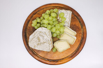 Assorted mouldy blue cheeses goats milk on a wooden chopping board with green grapes. White background