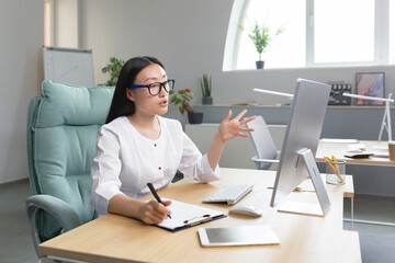 Young beautiful Asian female doctor consults patients remotely online consultation, woman works in office uses computer and web camera for video call.