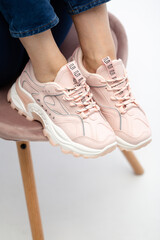 Female sneakers on legs. Pink woman's shoes on feet on chair. Sneakers close-up. Model in pink sneakers standing on chair