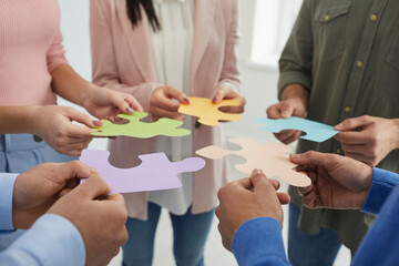 Obraz na płótnie Canvas Businesspeople joining puzzle pieces in office. Close up of people's hands holding colored pieces of puzzles symbolizing development and successful completion of tasks. Concept of business cooperation