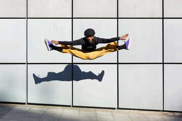 African American young adult man jumping energetically in the street. Dancer doing acrobatics in the city. Modern look, aesthetics Urban lifestyle. Space for text.