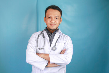 Portrait of an attractive confident male doctor, friendly smiling arms crossed wear white lab coat stethoscope isolated blue color background