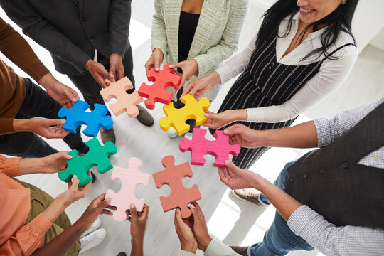 Cropped image of group of men and women standing in circle and connecting colored puzzle pieces. People learn to work together by taking business training course. Concept of cooperation. Top view.