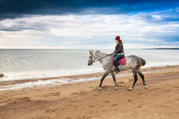 dressing jacket and jeans red-haired female rider hacks on a dappled steed along sandy beach