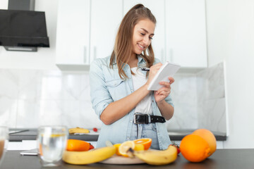 Healthy food concept. Young woman writes down the calorie content of products in notebook at kitchen