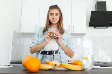 Young beautiful woman with a cup of coffee posing in the kitchen with many fruits. Healthy food concept