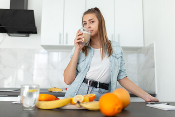 Young beautiful woman with a cup of coffee posing in the kitchen with many fruits. Healthy food concept