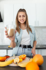 Young beautiful woman with a cup of coffee posing in the kitchen with many fruits. Healthy food concept